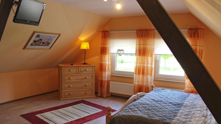A cozy bedroom with a double bed, a television, and a wooden wardrobe.
Large windows with bright curtains provide plenty of daylight.