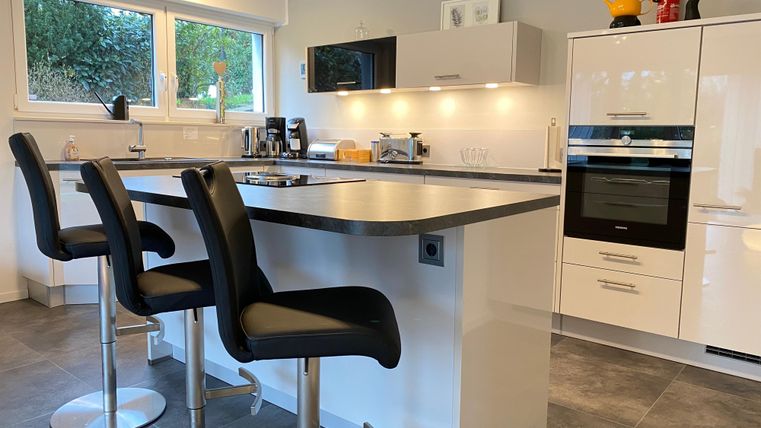 A modern kitchen with a large kitchen island table and high chair in minimalist design. Large windows provide plenty of natural light.