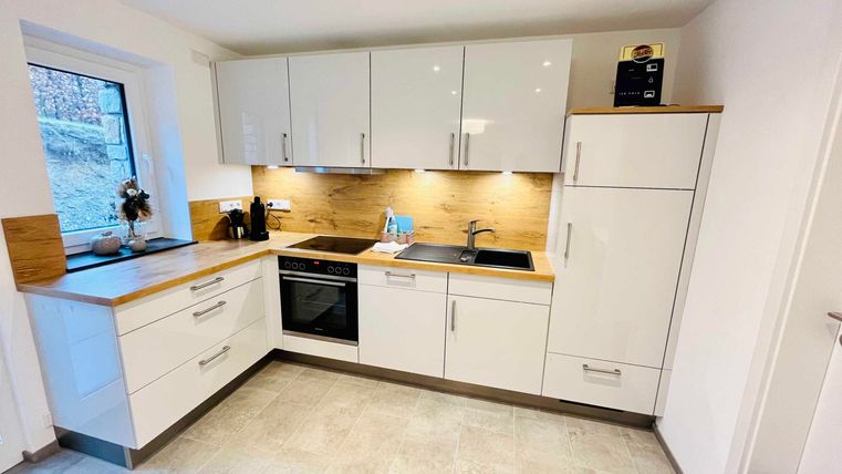 A modern kitchen with white furniture and wood accents. It features a sink, a stove, and a refrigerator.