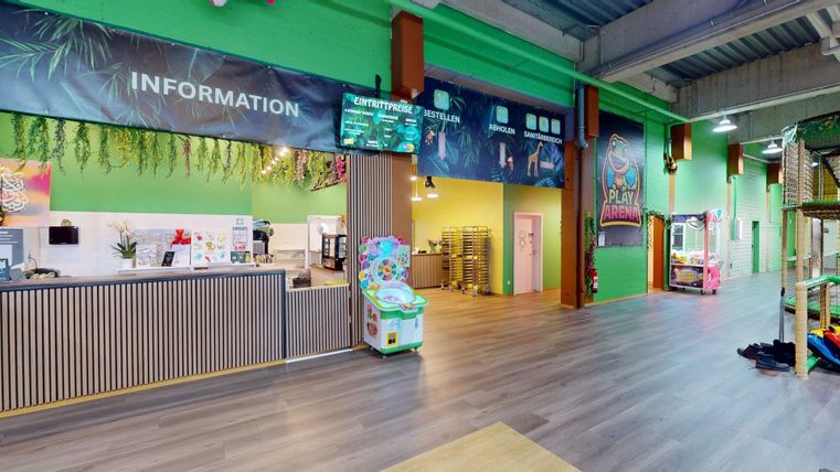 Ein bunter Innenraum mit einer Empfangstheke und Spielgeräten. Die Wände sind grün gestrichen, und es gibt verschiedene Informationsschilder.