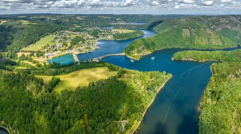 An airy view of a beautiful landscape with rivers and gentle hills. Green forests surround the waters and the small village on the shore.