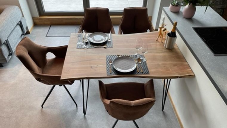 Een modern ontworpen eettafel van hout met vier stoelen. Op de tafel staan borden, glazen en een decoratieve vaas met verse bloemen.