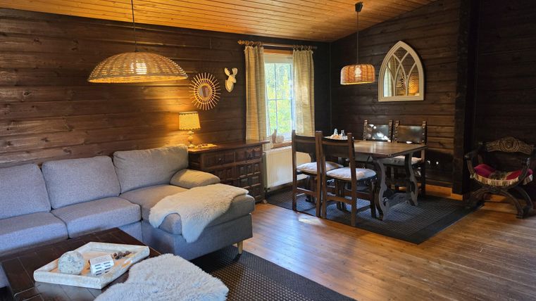 Een gezellig woonkamer met houten panelen, een comfortabele bank en een eettafel. Grote ramen laten veel licht binnen en creëren een uitnodigende sfeer.