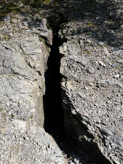 A deep fissure in the rock surrounded by stony ground. The image shows an impressive natural crack in the landscape.