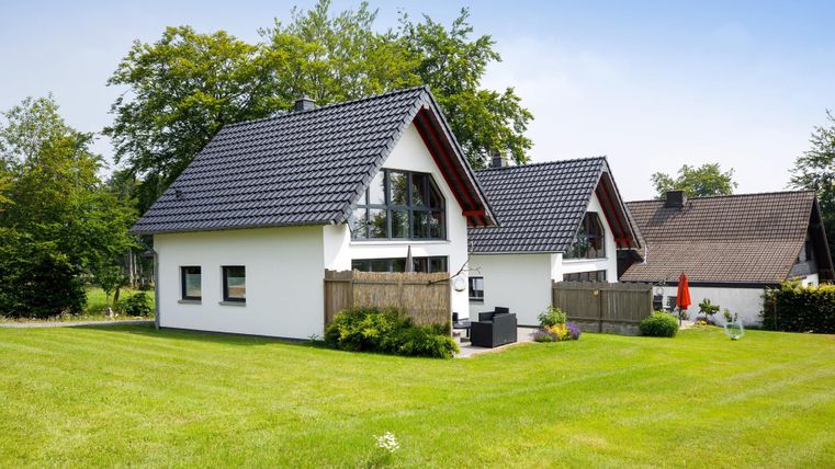 Two modern houses with gable roofs stand in a green environment. The garden is well-kept and offers an inviting outdoor area.