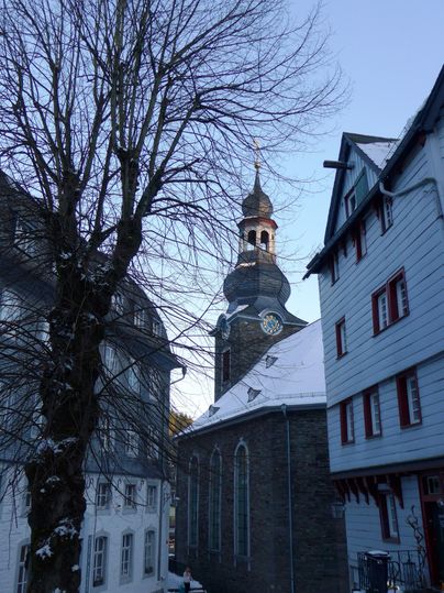A narrow alley with historic buildings and a church tower in the background. The scene is wintry and has a calm atmosphere.