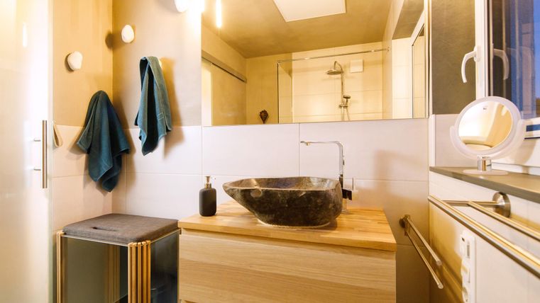 A modern bathroom with wooden details and an elegant washbasin. Towels hang on the wall, and there is a large window area for plenty of light.