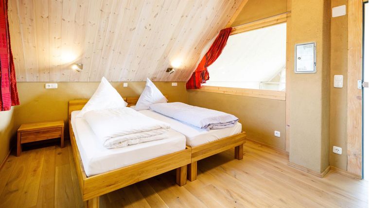 A cozy room with two single beds and wooden flooring. The walls are light and the windows let in plenty of light.
