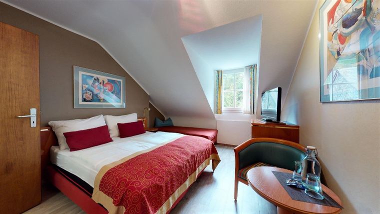 Een gezellige kamer met een dubbelbed, rode kussens en moderne decoratie. De grote ramen laten veel daglicht binnen en bieden een uitnodigend uitzicht.