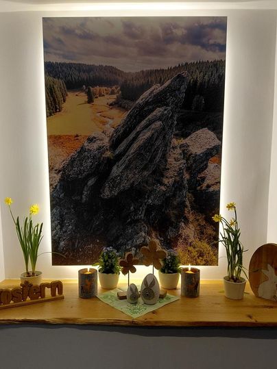 A beautiful wooden shelf with a landscape picture in the background. It holds flowers, candles, and Easter decorations.