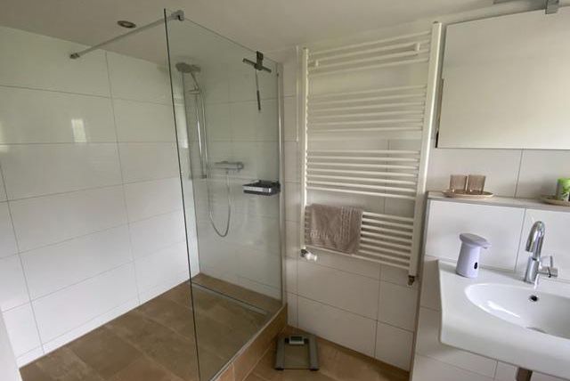 Een moderne badkamer met een glazen douche en een elegante wastafelmengkraan. De muren zijn betegeld in lichte, neutrale kleuren.