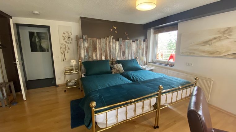 Een gezellige slaapkamer met twee eenpersoonsbedden en een gouden bedframe. De kamer heeft een warme houten vloer en ramen met uitzicht op de buitenlucht.