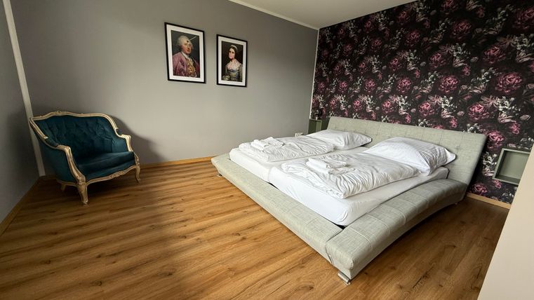 Een moderne slaapkamer met een groot bed en twee kussens. Aan de muur hangen twee schilderijen, en in de hoek staat een elegante stoel.