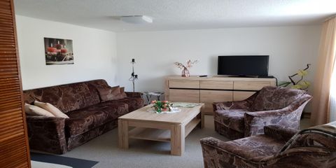 Een gezellige woonkamer met bruine banken en een houten salontafel. Aan de muur hangt een schilderij, en een televisie staat op de kast.
