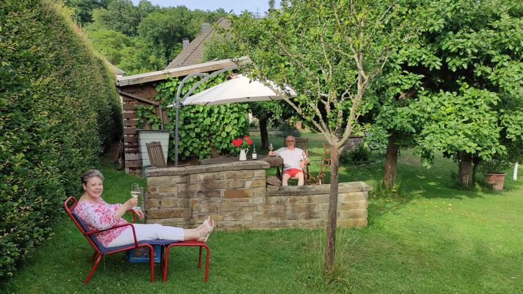 An inviting garden with two people sitting relaxed. In the background, there are trees and a pavilion.