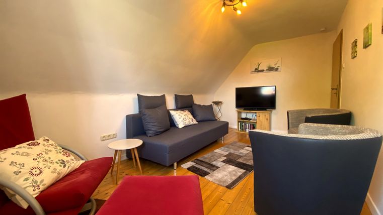 Een gezellige woonkamer met een blauwe bank en moderne stoelen. Er is een televisie en een houten vloer, wat een uitnodigende sfeer creëert.