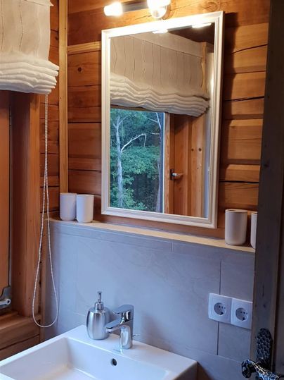 A modern bathroom with a white sink and a large mirror. The walls are made of wood and there is a window that lets light in.