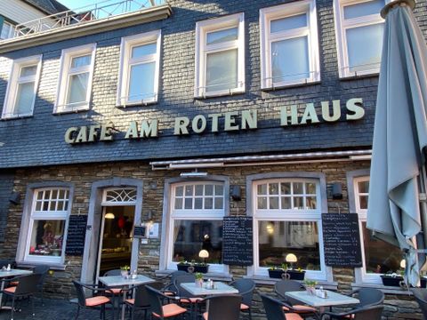 Een gezellig café genaamd "Café aan het Rode Huis". Er zijn tafels buiten en een uitnodigende sfeer.