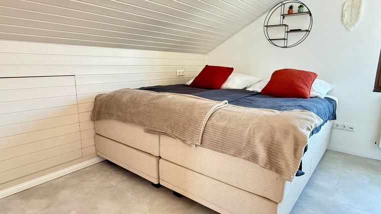 Een gezellige slaapkamer met een dubbel bed en rode kussens. Aan de muur hangen decoratieve elementen en het licht is helder.