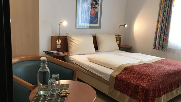 Een gezellige hotelkamer met een tweepersoonsbed en een klein tafeltje. Op de tafel staan waterflessen en glazen.
