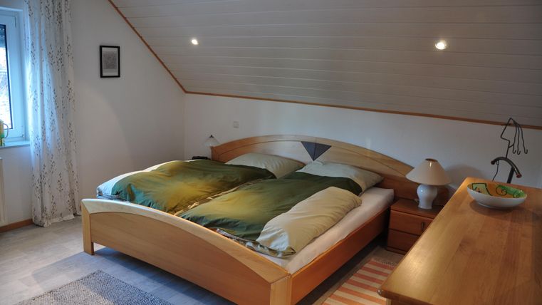 A cozy bedroom with a large double bed and wooden furniture. Warm colors and soft light create an inviting atmosphere.