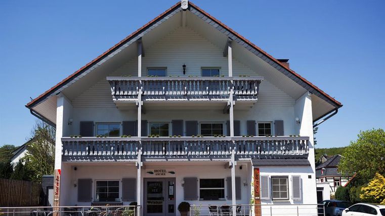 Een charmant hotelgebouw in Alpenstijl met twee balkons. De gevel is wit en de lucht is helder en blauw.
