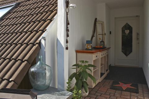An inviting entrance area with a bright door and a wooden table. Next to it are plants and a large glass container.