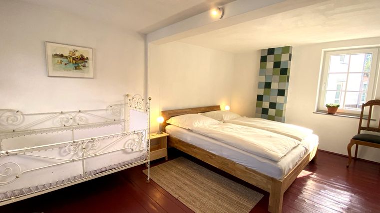Een gezellige slaapkamer met een dubbel bed en een kinderbed. De kamer heeft lichte muren en een houten vloer.