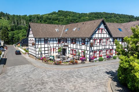 A charming half-timbered house on a quiet street. It is surrounded by green trees and adorned with blooming plants.