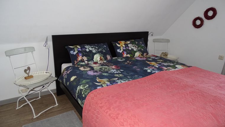 Een gezellige slaapkamer met een groot bed en bloemachtige kussens. Naast het bed staat een kleine tafel en een mooie decoratie aan de muur.