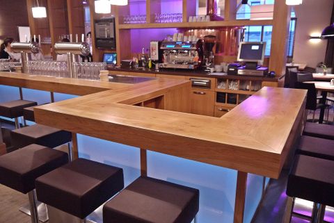 A modern bar with a wooden counter and stylish stools. The area is well-lit and has an inviting atmosphere.