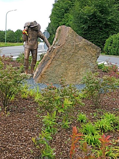 A statue of a diver interacting with a large stone. Surrounded by colorful plant arrangements.