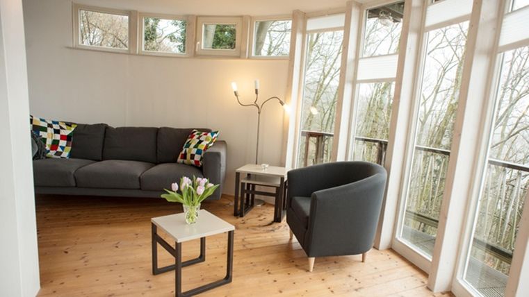 A cozy living space with a gray sofa and a black armchair. Fresh flowers are on the tables and large windows let in plenty of light.