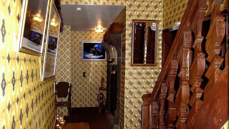 Ein Flur mit auffälliger, gelber Tapete und Holztreppe. An den Wänden hängen Bilder und es gibt ein kleines Möbelstück im Vordergrund.