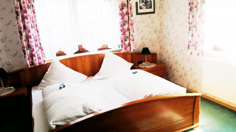 Een gezellige slaapkamer met een groot bed en bloemenpatronen op de muren. Heldere ramen zorgen voor een vriendelijke sfeer.