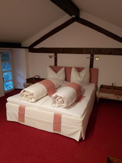 A cozy bedroom with a large bed and fresh towels. The walls are painted in soft colors, and the floor is covered with red carpet.