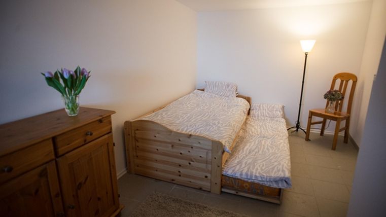 A simple room with two beds and a floor lamp. Fresh flowers are on a wooden cupboard.