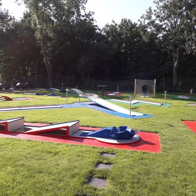 Ein bunt gestalteter Minigolfplatz mit verschiedenen Hindernissen. Die grüne Wiese und die Bäume im Hintergrund schaffen eine angenehme Atmosphäre.