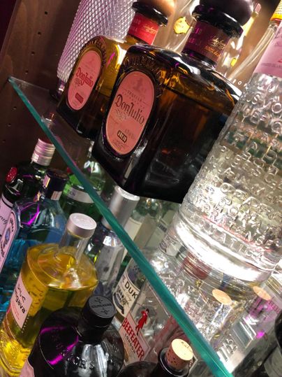 A selection of various spirits on a shelf. The bottles are arranged in different colors and shapes.
