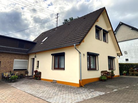 Een modern huis met een schuin dak en meerdere ramen. De ingang is geplaveid en versierd met planten.