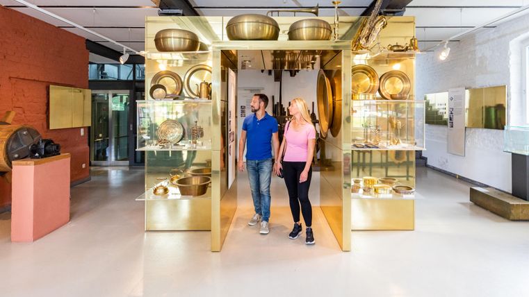 Een modern museum met glanzende vitrines die verschillende objecten tonen. Twee personen verkennen geïnteresseerd de tentoonstellingen.