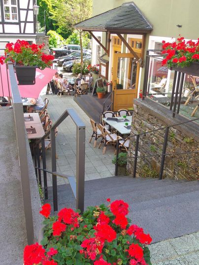 Een charmant restaurant met bloeiende rode geraniums en gezellige tafels buiten. De omgeving is groen en uitnodigend, ideaal voor ontspannen uren.