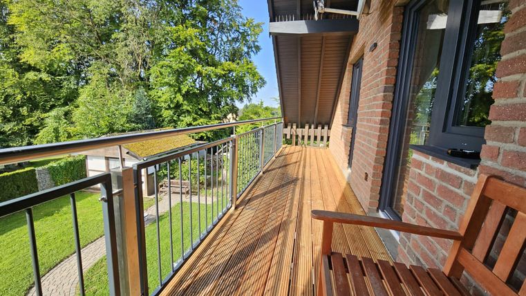 A sunny balcony with wooden planks and a beautiful view of the garden. The surroundings are green and inviting.
