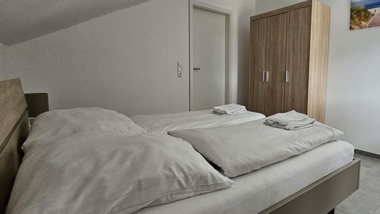 Een comfortabele slaapkamer met een tweepersoonsbed en frisse handdoeken. Op de achtergrond staat een houten kast naast een deur.