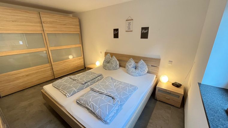 A modern bedroom with a double bed and two pillows. The furniture is made of light wood and there is soft lighting.