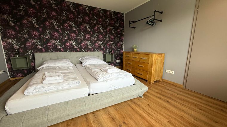 Een moderne slaapkamer met een comfortabel tweepersoonsbed en een houten kast. De muren zijn versierd met een bloemmotief, en de vloer is van hout.