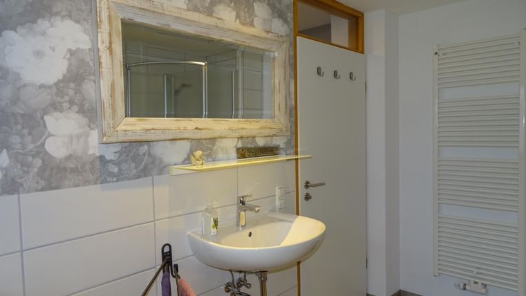 Een moderne badkamer met een wastafel en een grote spiegel. De muren zijn versierd met een stijlvol, grijs patroon.