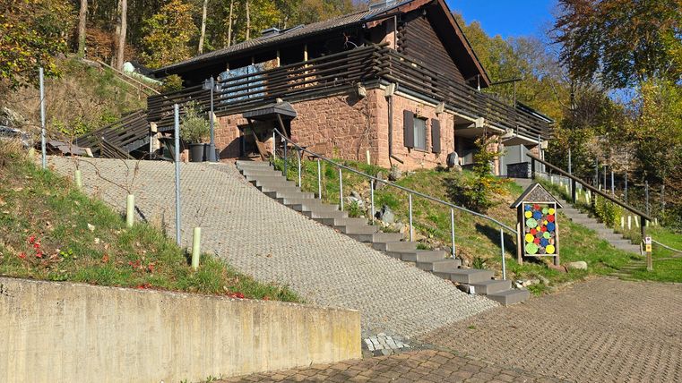 A cozy house on a hill, surrounded by trees. The blue sky and sunny surroundings give the scene a friendly impression.