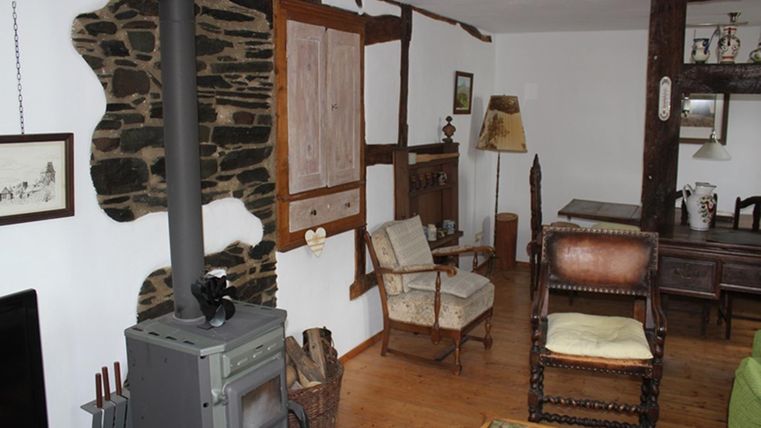 A cozy living space with a wood stove and rustic furniture. The walls are partially paneled with stone and wood.
