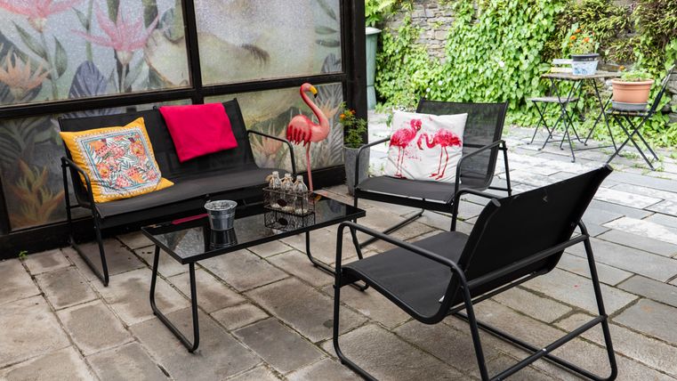 A cozy outdoor seating area with black garden furniture and colorful cushions. Surrounded by plants and a charming stone terrace.